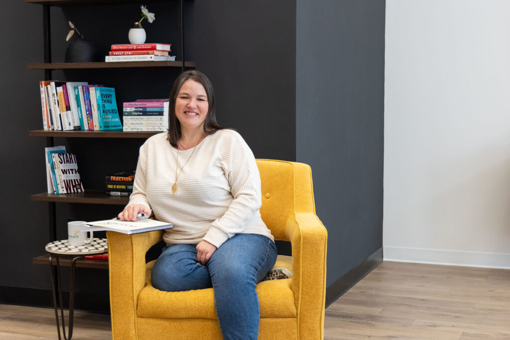 Heather Deveaux sitting in a yellow chair against a book shelf