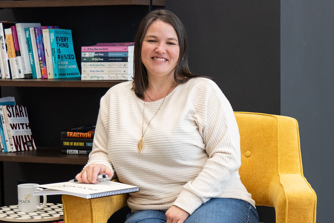 Heather Deveaux sitting in a yellow chair against a book shelf