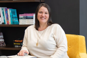 Heather Deveaux sitting in a yellow chair against a book shelf